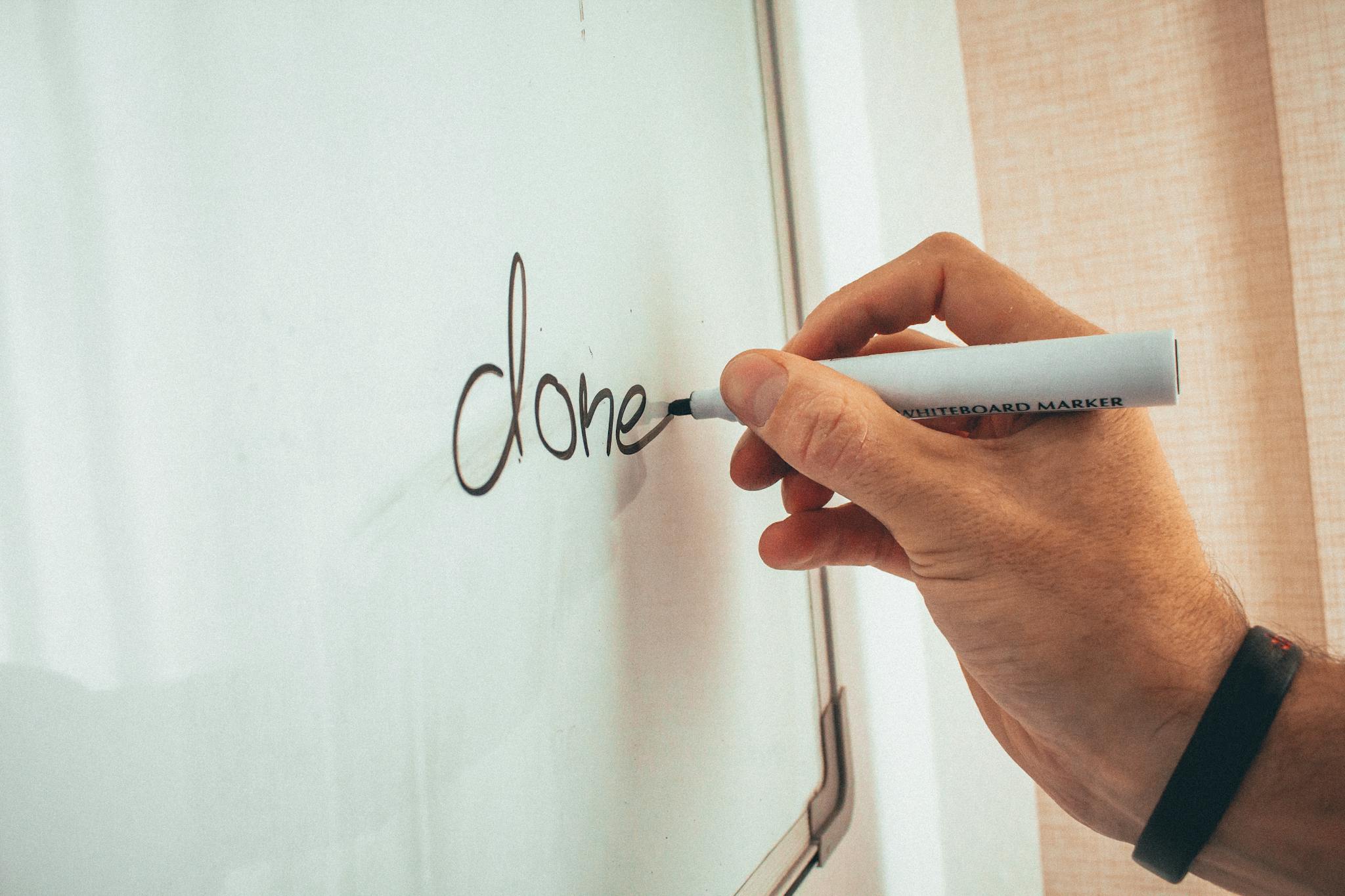 Crop unrecognizable male coach writing done word on whiteboard during presentation in light office